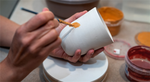 Stock image of painting a orange glaze onto an unfinished pottery mug