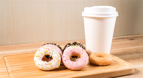 Generic image of a white disposable coffee cup sitting on a board next to a handful of colorful dounts