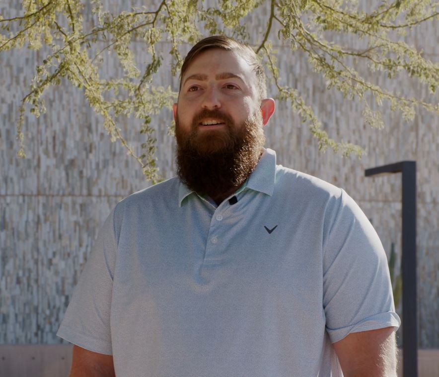 Bearded man with brown hair and blue shirt smiling happily.