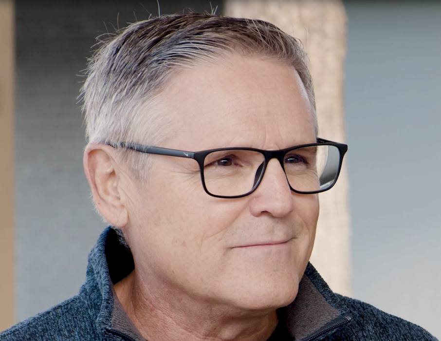 A man wearing glasses with short white and grey hair and a grey shirt.