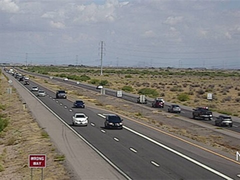 A highway in a desert landscape with a clear sky. Cars travel in both directions. A 