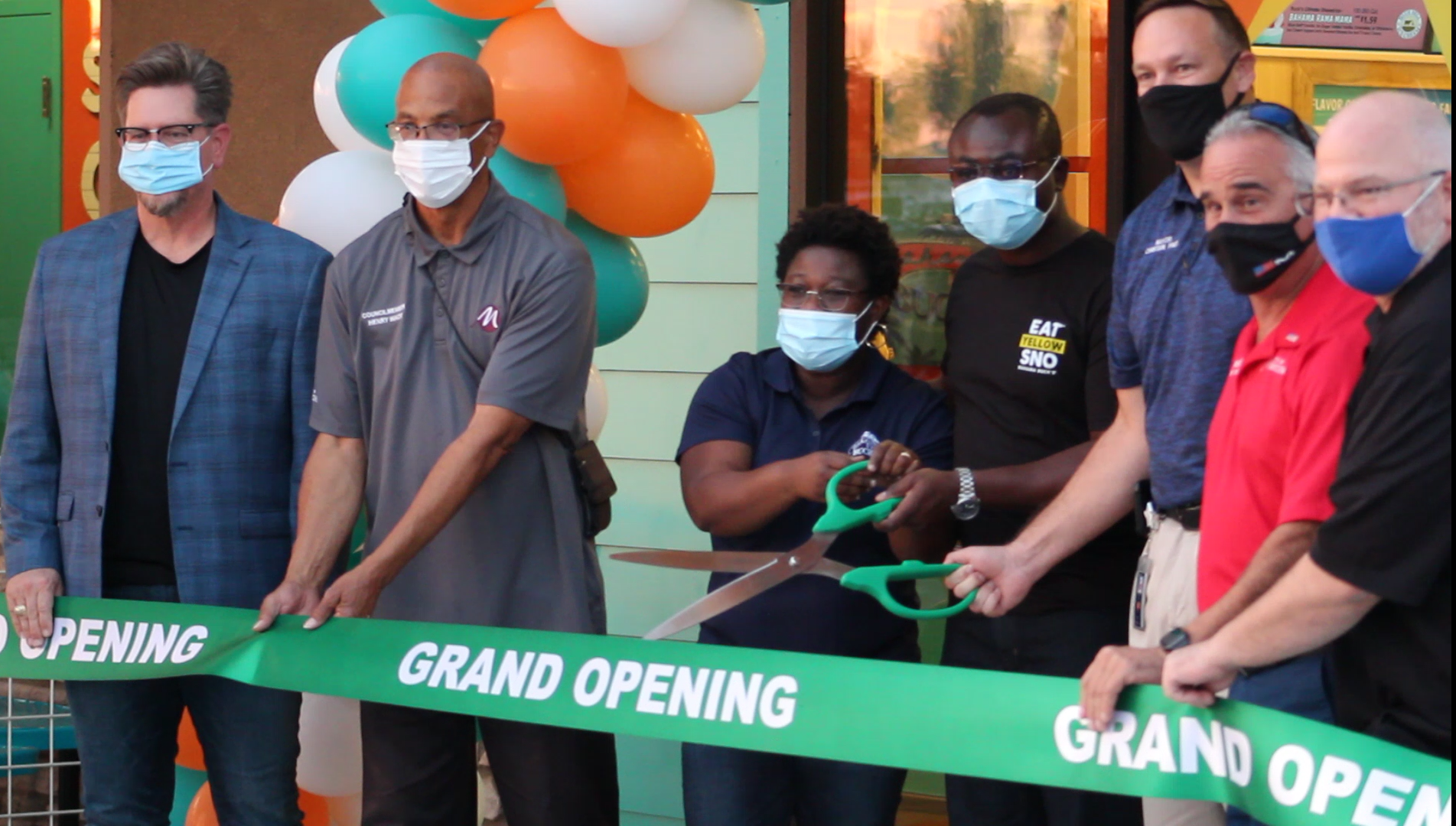 A group of people wearing masks stand behind a green 