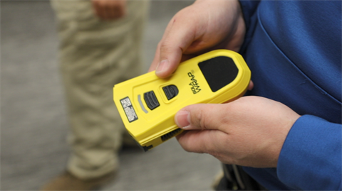 Person holds a bright yellow electronic device with a screen, labeled 