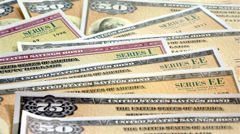 A stack of various U.S. savings bonds, including Series I and EE, with denominations and text visible. The bonds display vintage, intricate designs.