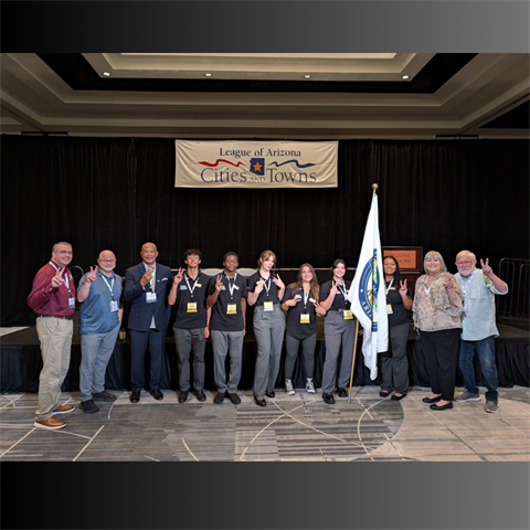 A diverse group of people stands on stage under a 