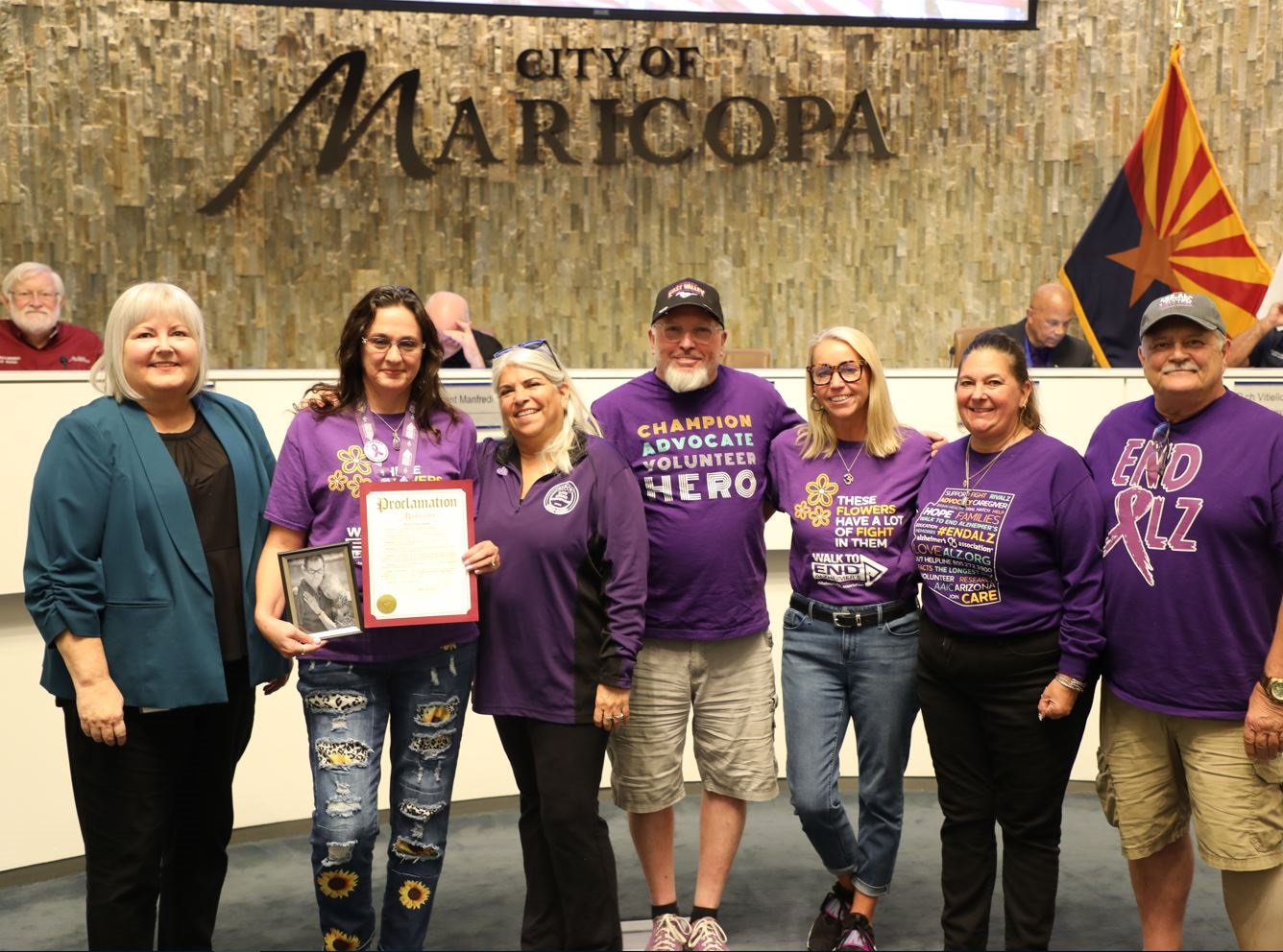 A group of people wearing purple shirts stand together in front of a 