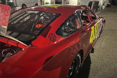 Red race car parked in a dimly lit pit area. The car's number 