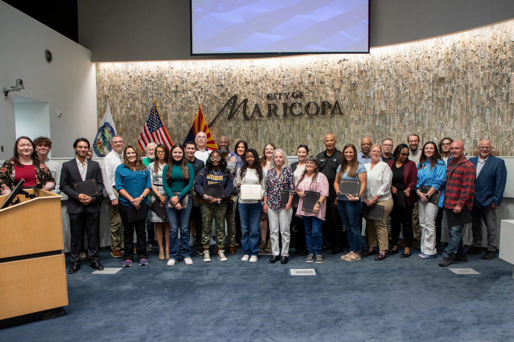 A diverse group of around 30 people stands smiling in front of a wall with 