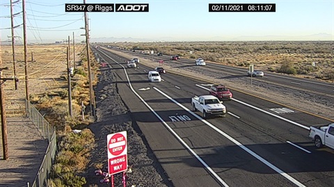 Desert highway scene showing vehicles traveling on a multi-lane road under a clear blue sky, with a 