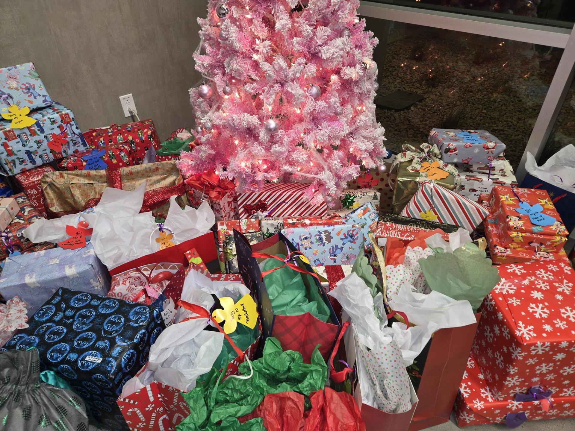 A pink Christmas tree surrounded by a variety of wrapped gifts in festive paper and bags, creating a joyful and festive atmosphere.