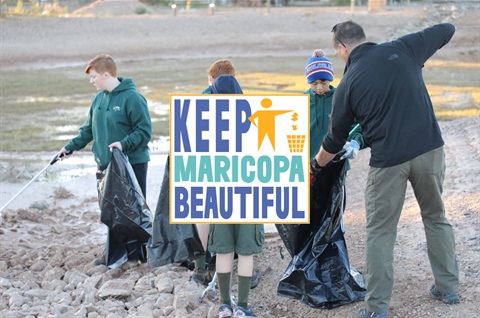 A group of people in green hoodies clean up litter in an outdoor area with rocks and dirt. They use trash bags and pickers. Logo reads 
