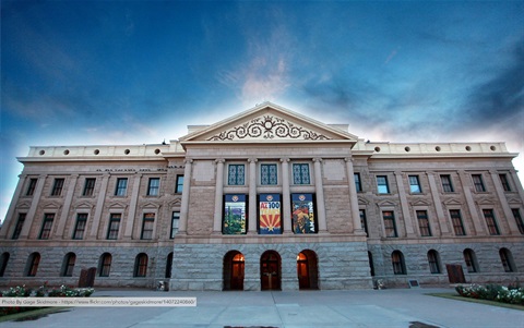 A grand historical building with a classical facade under a vibrant dusk sky. The architecture includes columns and commemorative banners.