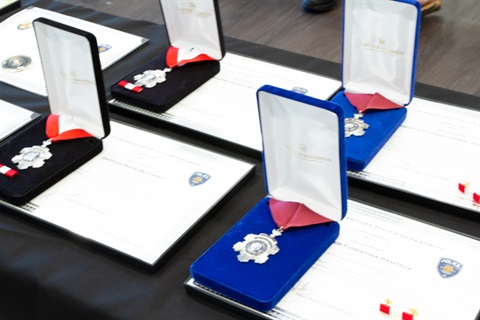Medals in blue velvet cases with white lining rest on certificates displayed on a table. The scene conveys achievement and recognition.