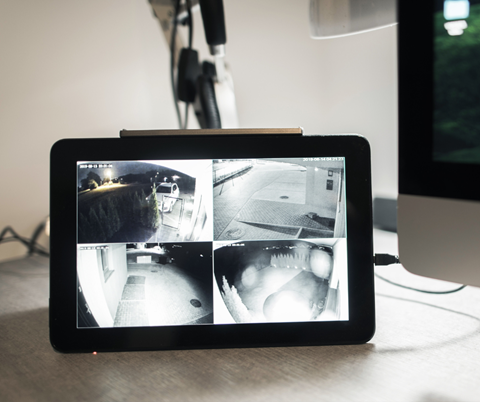 A tablet displays a split-screen view from four security cameras, showing various outdoor night scenes. The setting feels secure and monitored.