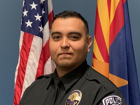 A police officer in uniform stands confidently in front of American and Arizona flags, conveying a sense of duty and pride.