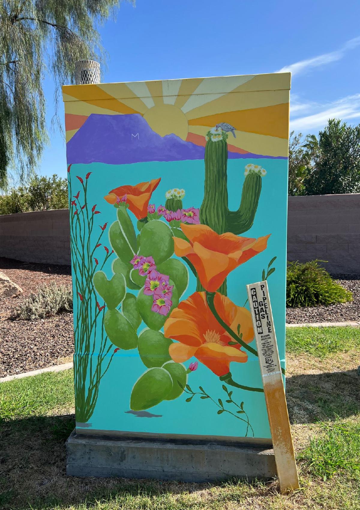 Utility box mural featuring vibrant desert scene with cactus, poppies, and mountains. A sun rises in the background. Tone is colorful and lively.