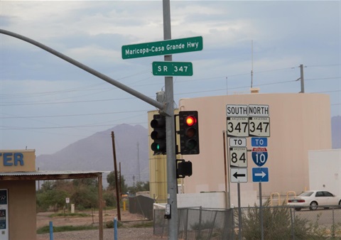 Traffic light at red, with highway signs for Maricopa-Casa Grande Hwy and SR 347. Background shows distant mountains and overcast sky.