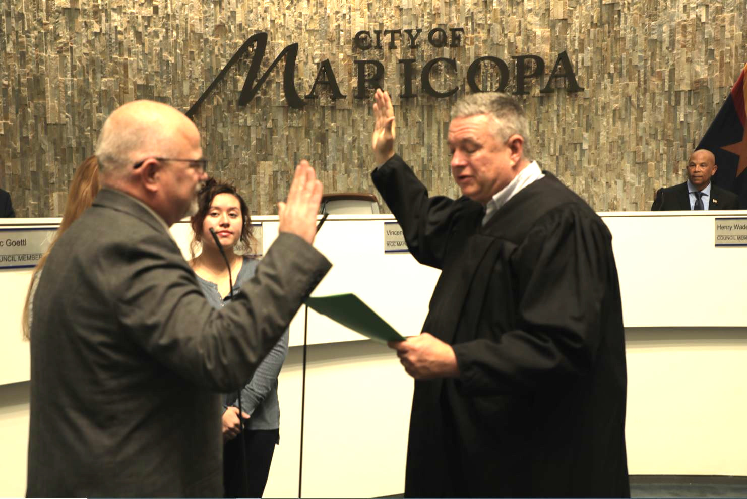 A man in a suit is sworn in by a judge at a city council meeting in Maricopa. People watch in the background, creating a formal atmosphere.