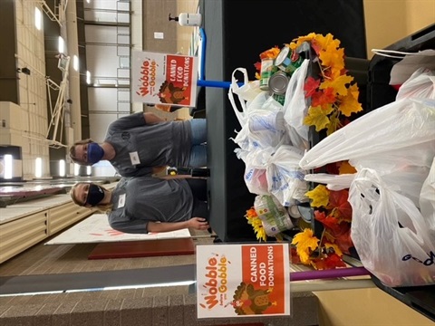 A decorated box filled with canned food sits in front of a table where two masked women stand. Signs read 