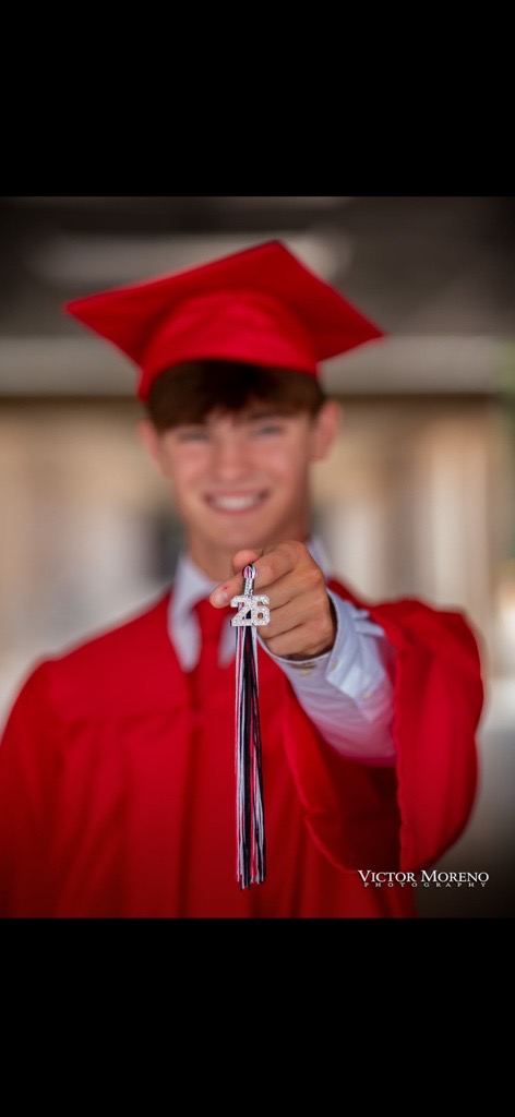 Young graduate in red attire, smiling and holding a tassel with 