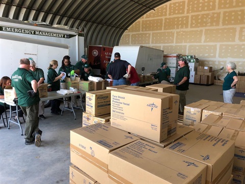 Volunteers in green shirts organize supplies in a large warehouse with 