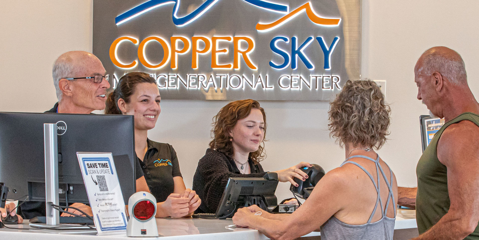 People at a reception desk in Copper Sky Recreational Center, engaging warmly with visitors. The atmosphere is welcoming and lively.
