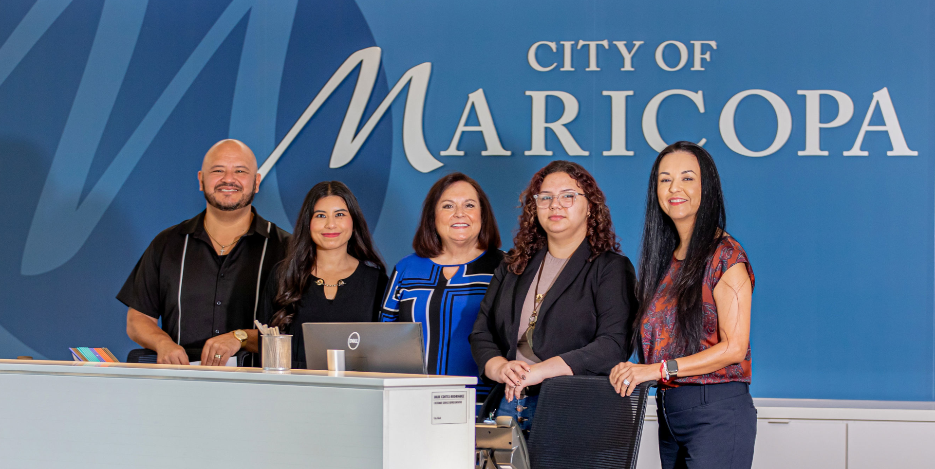 Five people stand smiling behind a modern reception desk with a blue backdrop reading 