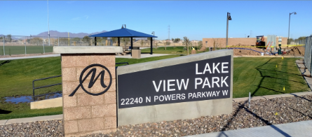 Sign for Lake View Park with a logo and address. A sunny park scene in the background with a pavilion, green grass, and mountains in the distance.