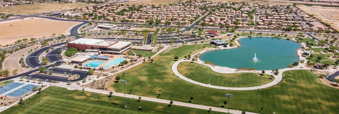 Scenic shot of an outdoor sports complex with aquatics center pool, amphitheater, lake, and green grass in front of a suburban community