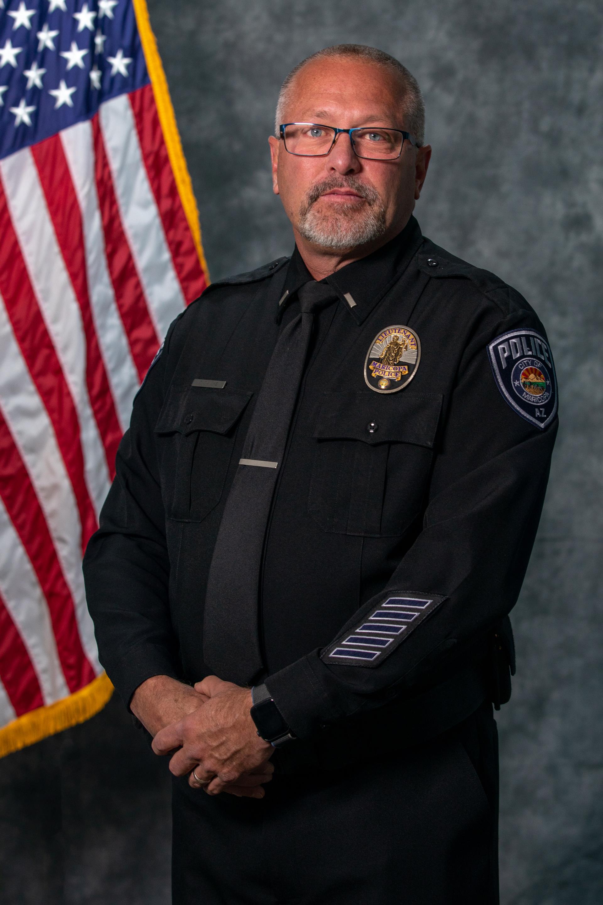 A police officer in uniform stands confidently against a gray background with an American flag to the left. The officer exudes professionalism and authority.