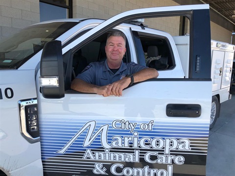 A man in a uniform smiles while leaning on an open truck door labeled 