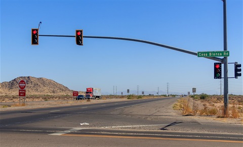 A desert highway intersection with traffic lights showing red, a road sign reading 