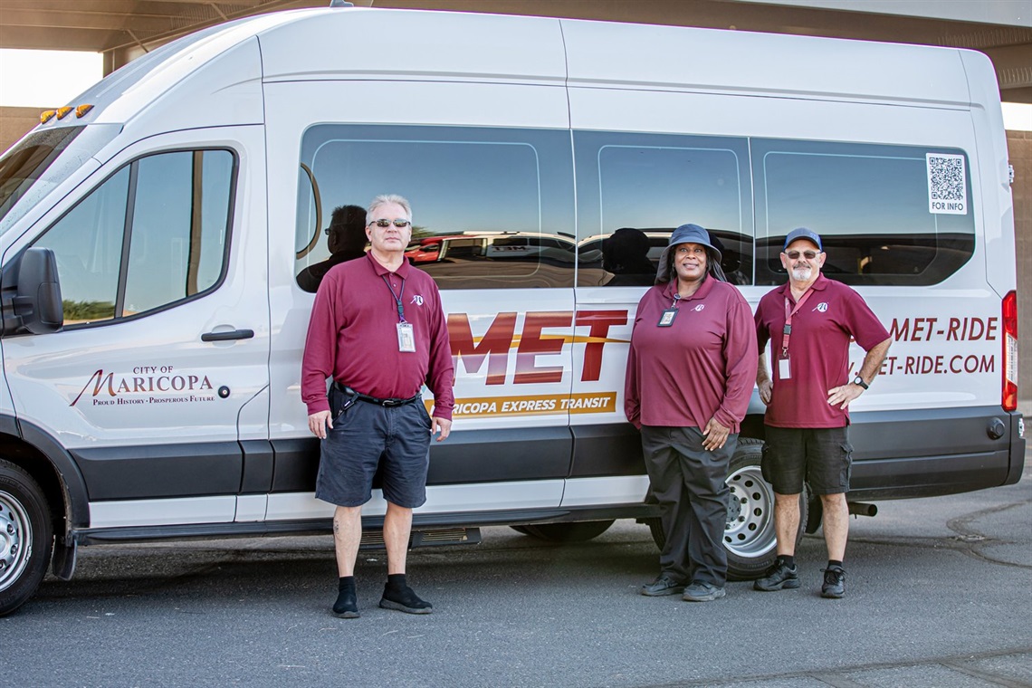 Photograph of three individuals in maroon shirts and black shorts in front of a white bus with the Maricopa Express Transit logo on the side